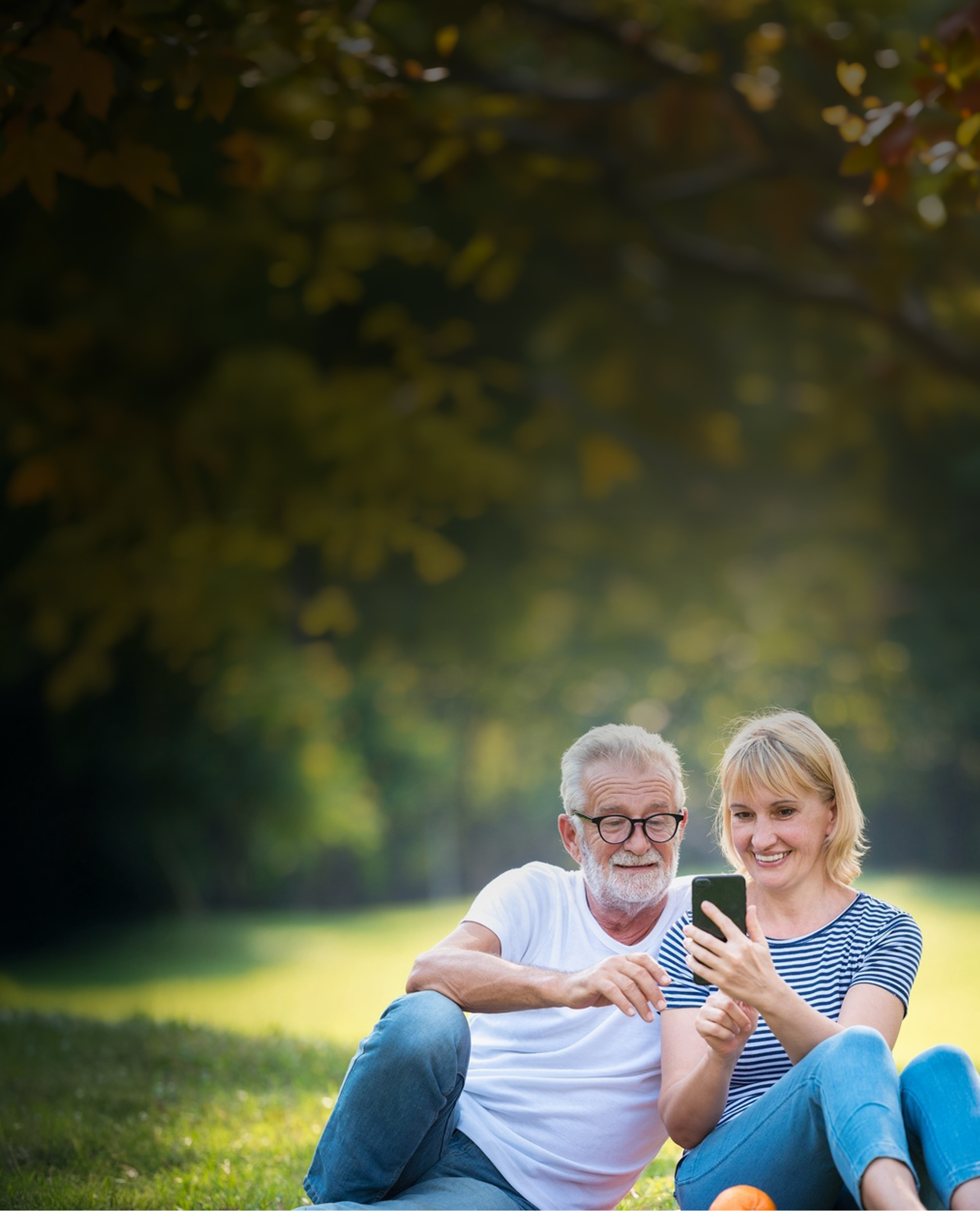 mature couple sitting in park on a sunny day looking at a mobile phone and smiling